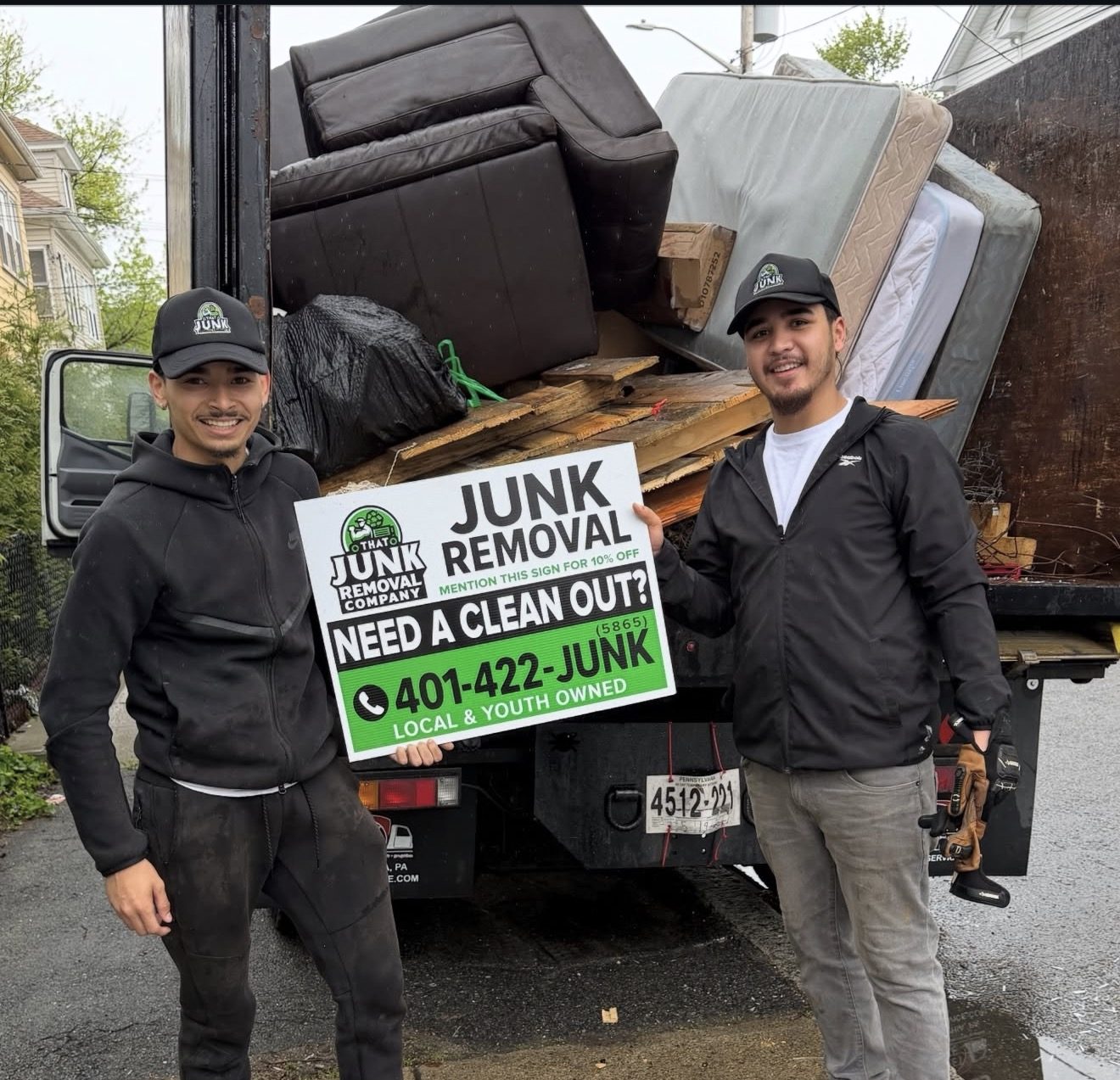 Two crew members with a Need A Clean Out sign in front of a fully loaded truck